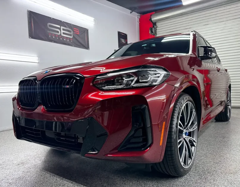 Deep red BMW X3 M parked inside a detailing studio, with polished paint and blacked-out kidney grilles reflecting the lighting.
